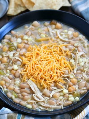 Black bowl filled with white chicken chili and topped with shredded cheese.