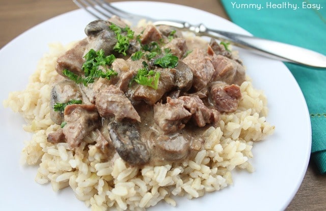 White plate with brown rice topped with beef stroganoff.