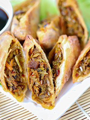 A white plate with several egg rolls, cut in half, showing cooked veggies inside.