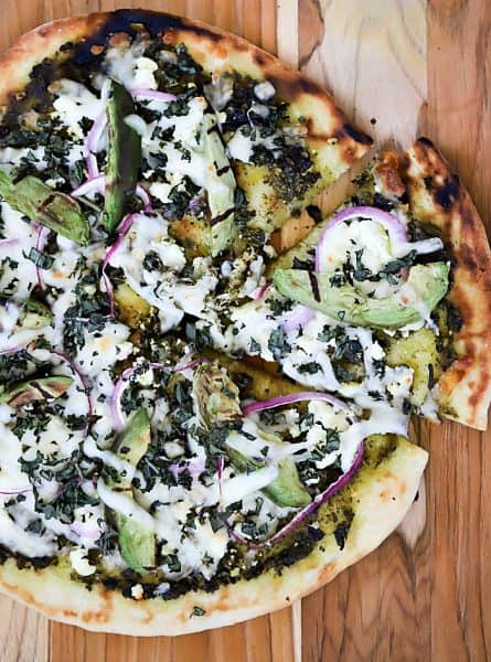 Overhead view of finished grilled pizza with a slice pulled slightly out.