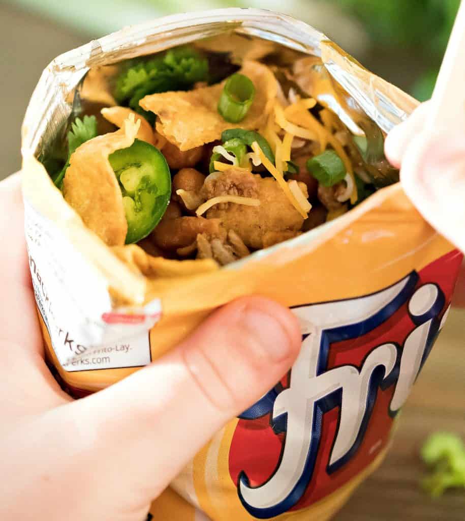 Frito bag filled with ground meat and beans with taco toppings and a fork.
