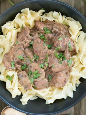 Black plate filled with egg noodles and topped with beef stroganoff. Square overhead picture.