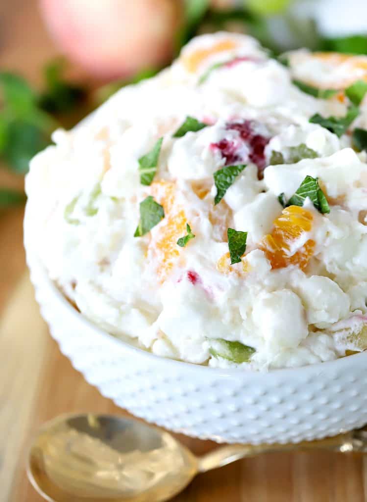 White bowl filled with fruit salad and a gold spoon.
