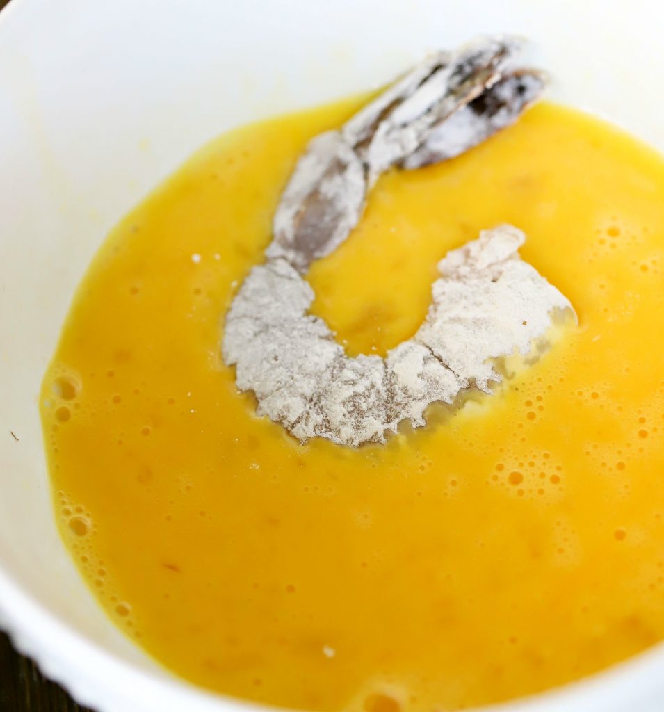 Flour coated shrimp being dipped in an egg wash.