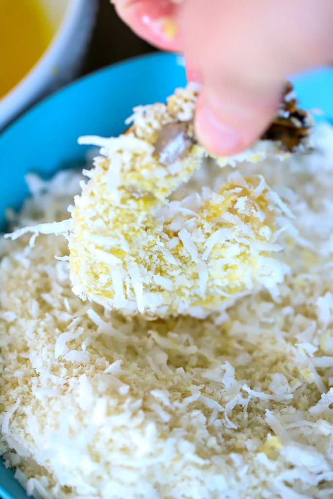 Egg washed shrimp being dipped in a panic and coconut mixture.