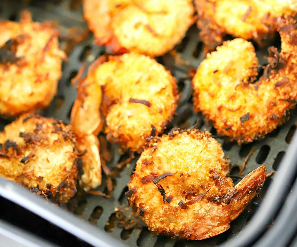 Air fryer basket with cooked coconut shrimp inside