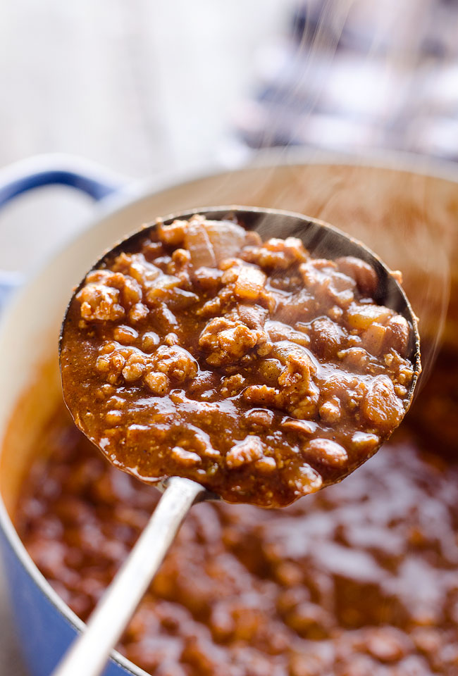 A big scoop of chili from a cast iron pot.