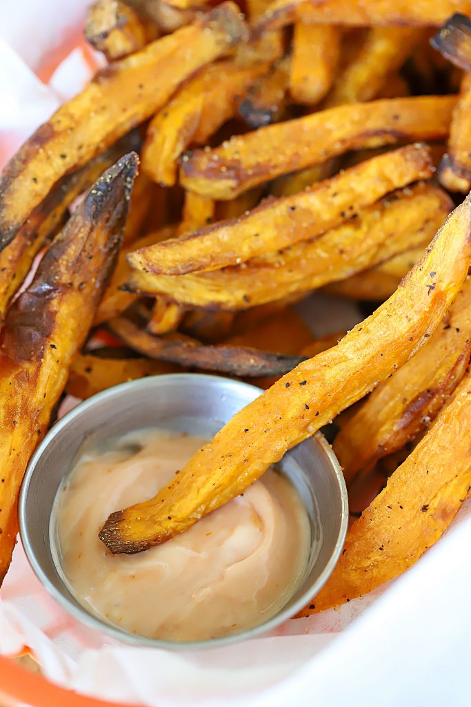 Big pile of French fries with dip in the middle.