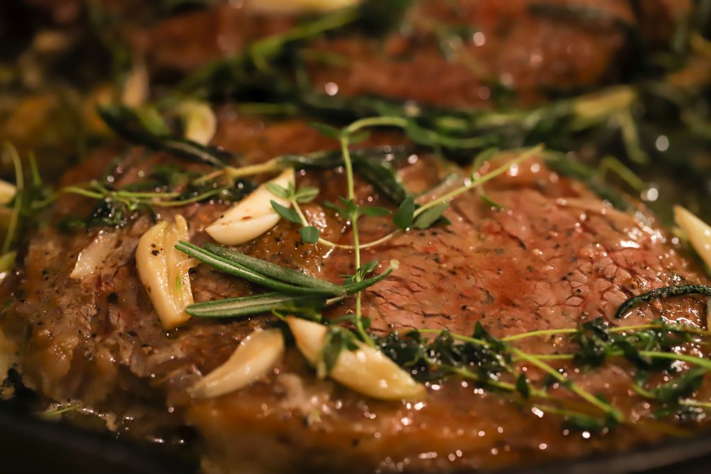 Close up of delicious steak topped with garlic, rosemary & thyme.